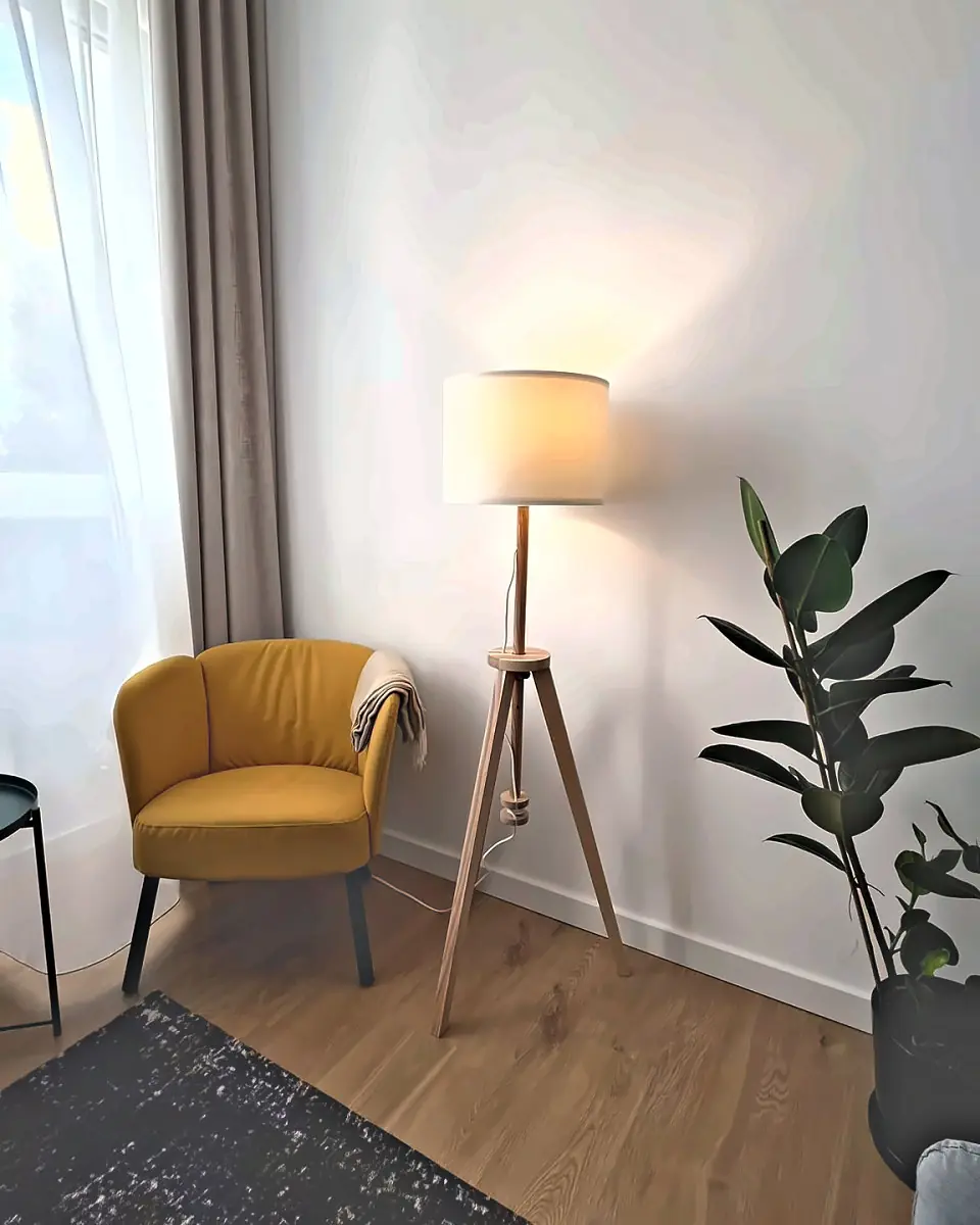 Żółty fotel z kocem, lampa stojąca i fikus